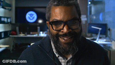 A Man With Glasses And A Beard Is Smiling In Front Of A Screen That Says U.s. Navy GIF