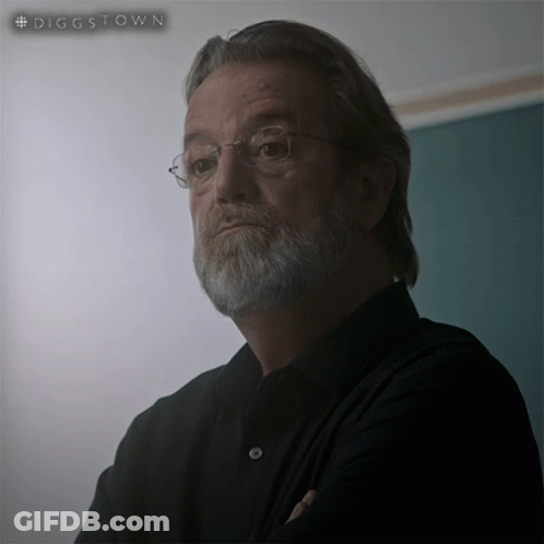 A Man With Glasses And A Beard Is Standing In Front Of A Green Board That Says #Diggstown GIF