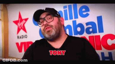 A Man With Glasses And A Beard Is Standing In Front Of A Virgin Radio Sign GIF