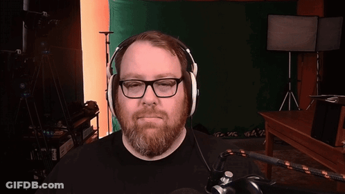 A Man With Glasses And A Beard Is Wearing Headphones In Front Of A Green Screen GIF