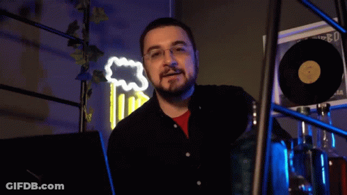 A Man With Glasses And A Beard Says " Scappa " In Front Of A Neon Sign GIF