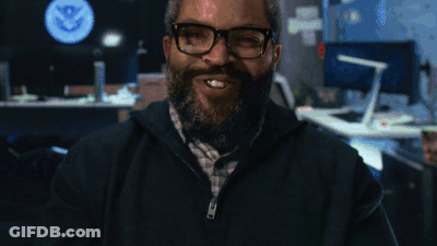 A Man With Glasses And A Beard Smiles In Front Of A U.s. Department Of State Logo GIF