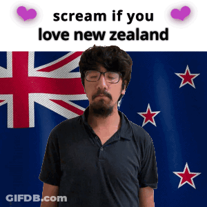 A Man With Glasses And A Beard Stands In Front Of A New Zealand Flag GIF