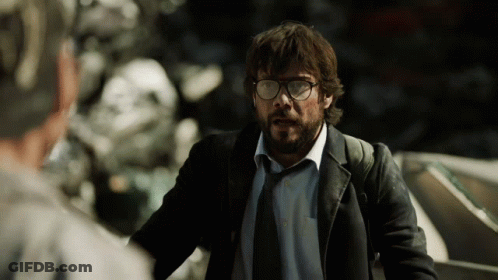 A Man With Glasses And A Beard Stands In Front Of A Pile Of Junk GIF