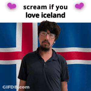 A Man With Glasses And A Beard Stands In Front Of An Iceland Flag GIF