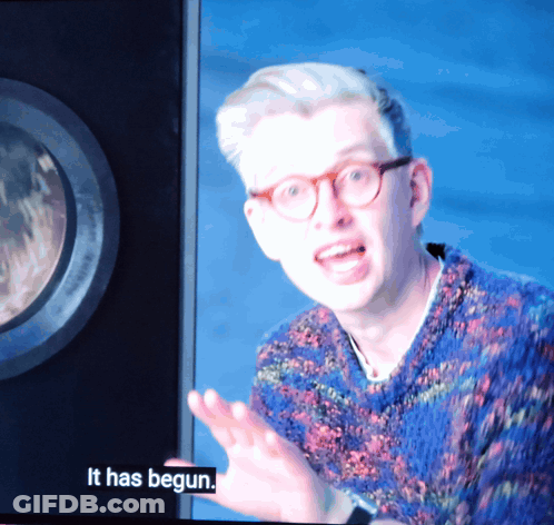 A Man With Glasses And A Blue Sweater Says It Has Begun On A Screen GIF