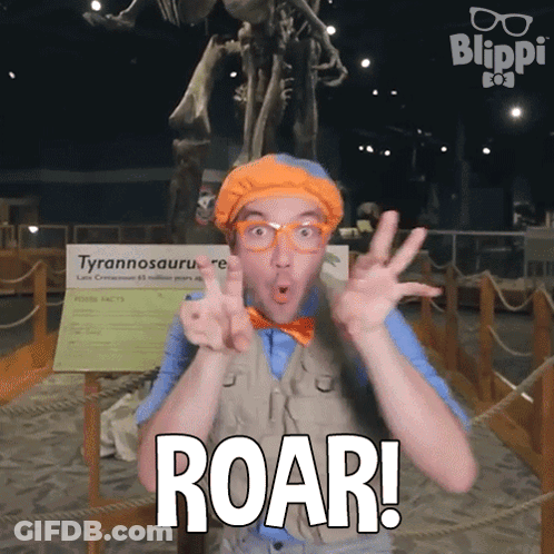 A Man With Glasses And A Bow Tie Says Roar In Front Of A Dinosaur Skeleton GIF