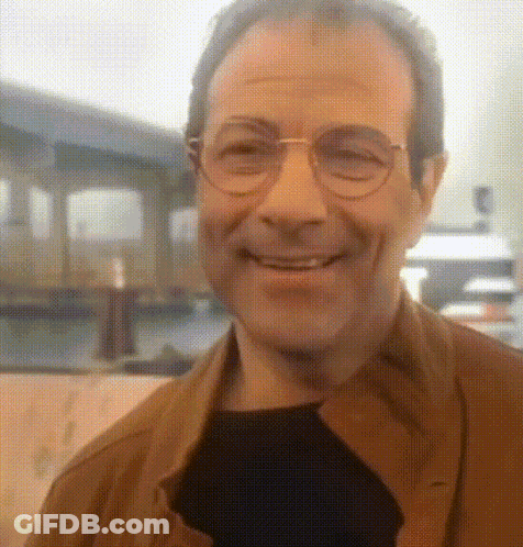 A Man With Glasses And A Brown Jacket Is Smiling GIF