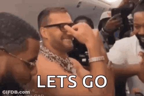 A Man With Glasses And A Chain Around His Neck Is Covering His Nose With His Hand And The Words `` Lets Go '' Are Visibl GIF