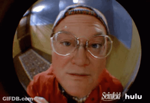 A Man With Glasses And A Hat Is Looking Through A Peephole With Seinfeld Hulu Written On It GIF