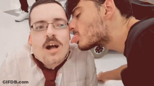A Man With Glasses And A Mustache Is Kissing Another Man On The Cheek GIF