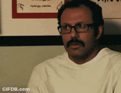Man With Glasses And Mustache Sitting In Front Of Sign GIF