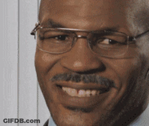 A Man With Glasses And A Mustache Is Smiling And Looking At The Camera GIF
