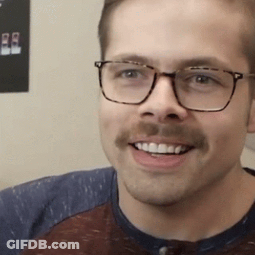 A Man With Glasses And A Mustache Is Smiling And Wearing A Shirt . GIF