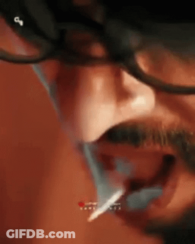 A Man With Glasses And A Mustache Is Smoking A Cigarette With A Lighter In His Mouth . GIF