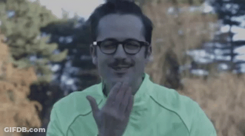 A Man With Glasses And A Mustache Is Wearing A Green Jacket And Making A Face . GIF