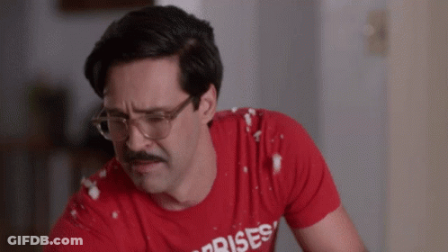 A Man With Glasses And A Mustache Is Wearing A Red Shirt That Says Surprises GIF