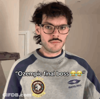 A Man With Glasses And A Mustache Is Wearing A Sweatshirt That Says Ozempic Final Boss GIF