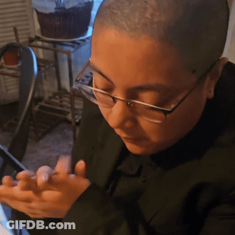 A Man With Glasses And A Shaved Head Looks At His Phone GIF
