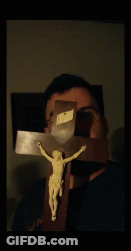 A Man With Glasses Holds A Crucifix In Front Of His Face GIF
