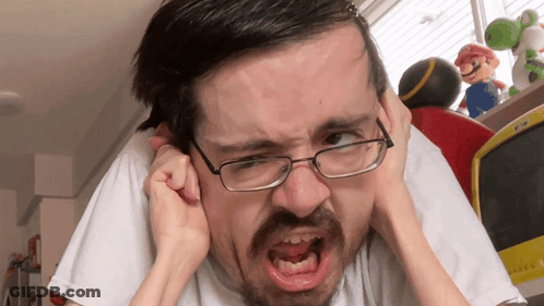 A Man With Glasses Is Covering His Ears With His Hands And Making A Funny Face GIF