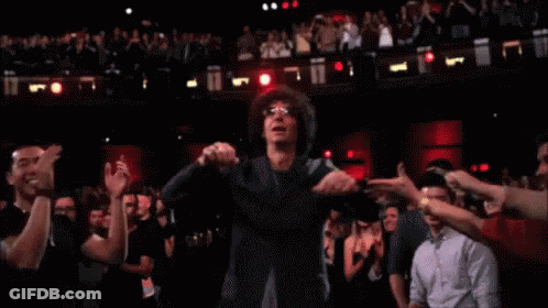 A Man With Glasses Is Dancing In Front Of A Crowd Of People GIF
