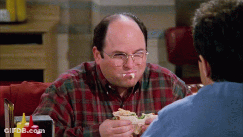 A Man With Glasses Is Eating A Sandwich While Another Man Watches GIF