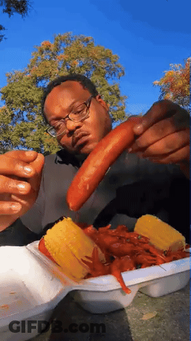 A Man With Glasses Is Eating Corn On The Cob And Crayfish GIF