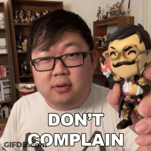 A Man With Glasses Is Holding A Figurine That Says " Do N't Complain " On It GIF
