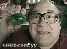 A Man With Glasses Is Holding A Green Egg That Says Patty 'S Putts On It GIF