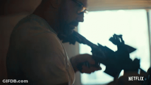 Man With Glasses Holding Gun In Front Of Window GIF