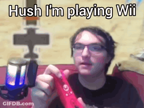 A Man With Glasses Is Holding A Red Wii Controller And Says " Hush I 'M Playing Wii " GIF