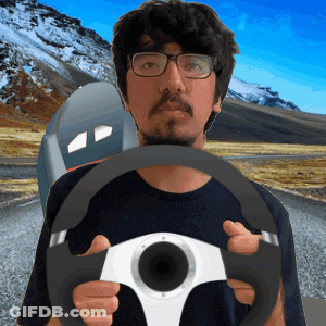 A Man With Glasses Is Holding A Steering Wheel In Front Of A Mountain GIF