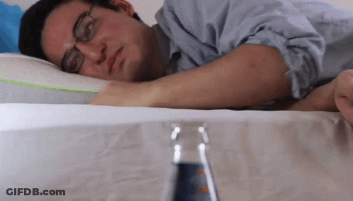 A Man With Glasses Is Laying On A Bed With A Bottle Of Soda In Front Of Him GIF