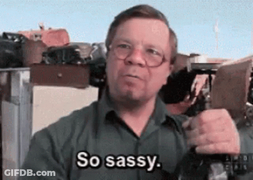A Man With Glasses Is Saying So Sassy While Holding A Gun GIF