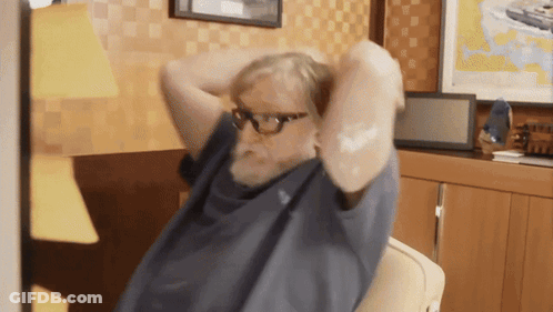 A Man With Glasses Is Sitting In A Chair With His Arms Behind His Head GIF