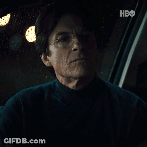 A Man With Glasses Is Sitting In A Dark Room With A Hbo Logo In The Corner GIF