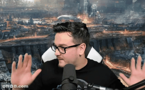 A Man With Glasses Is Sitting In Front Of A Microphone With His Hands Outstretched GIF