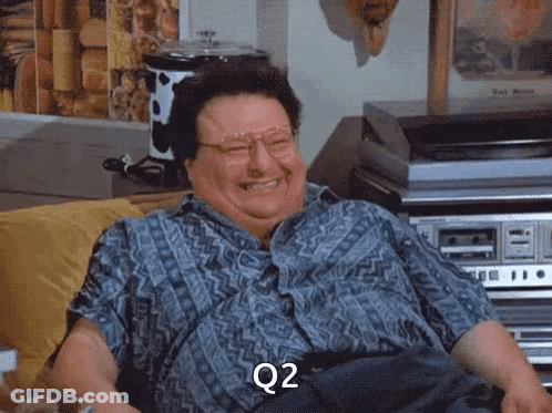 A Man With Glasses Is Sitting On A Couch And Laughing With The Word Q2 On His Face GIF