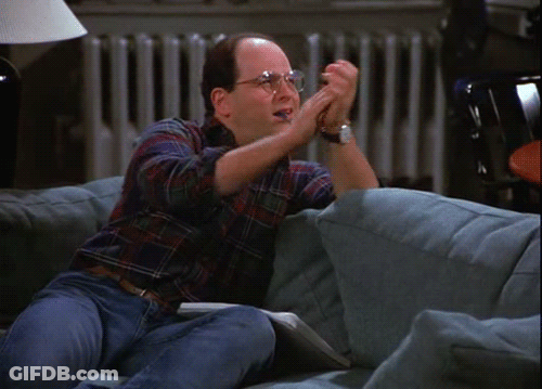 A Man With Glasses Is Sitting On A Couch With His Hands In The Air GIF