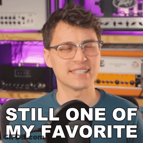 A Man With Glasses Is Smiling In Front Of A Microphone And Says " Still One Of My Favorite " GIF