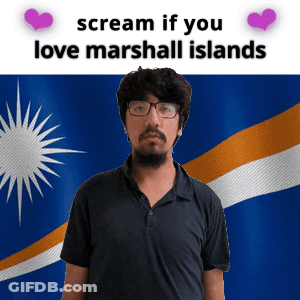 A Man With Glasses Is Standing In Front Of A Flag That Says " Scream If You Love Marshall Islands " GIF