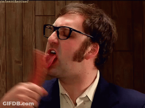 A Man With Glasses Is Sticking His Tongue Out While Eating Something GIF