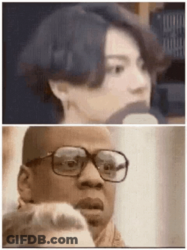 A Man With Glasses Is Talking Into A Microphone Next To A Woman . GIF