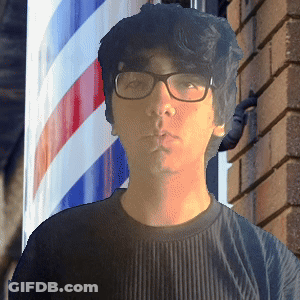 A Man With Glasses Stands In Front Of A Barber Pole GIF