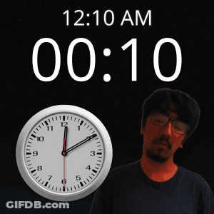 A Man With Glasses Stands In Front Of A Clock That Reads 12:10 Am GIF