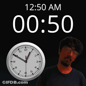 A Man With Glasses Stands In Front Of A Clock That Reads 12:50 Am GIF