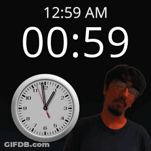 A Man With Glasses Stands In Front Of A Clock That Reads 12:59 Am GIF