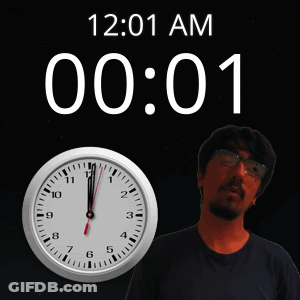 A Man With Glasses Stands In Front Of A Clock That Says 12:01 Am GIF