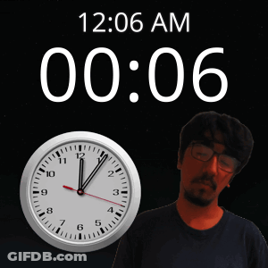 A Man With Glasses Stands In Front Of A Clock That Says 12:06 Am GIF